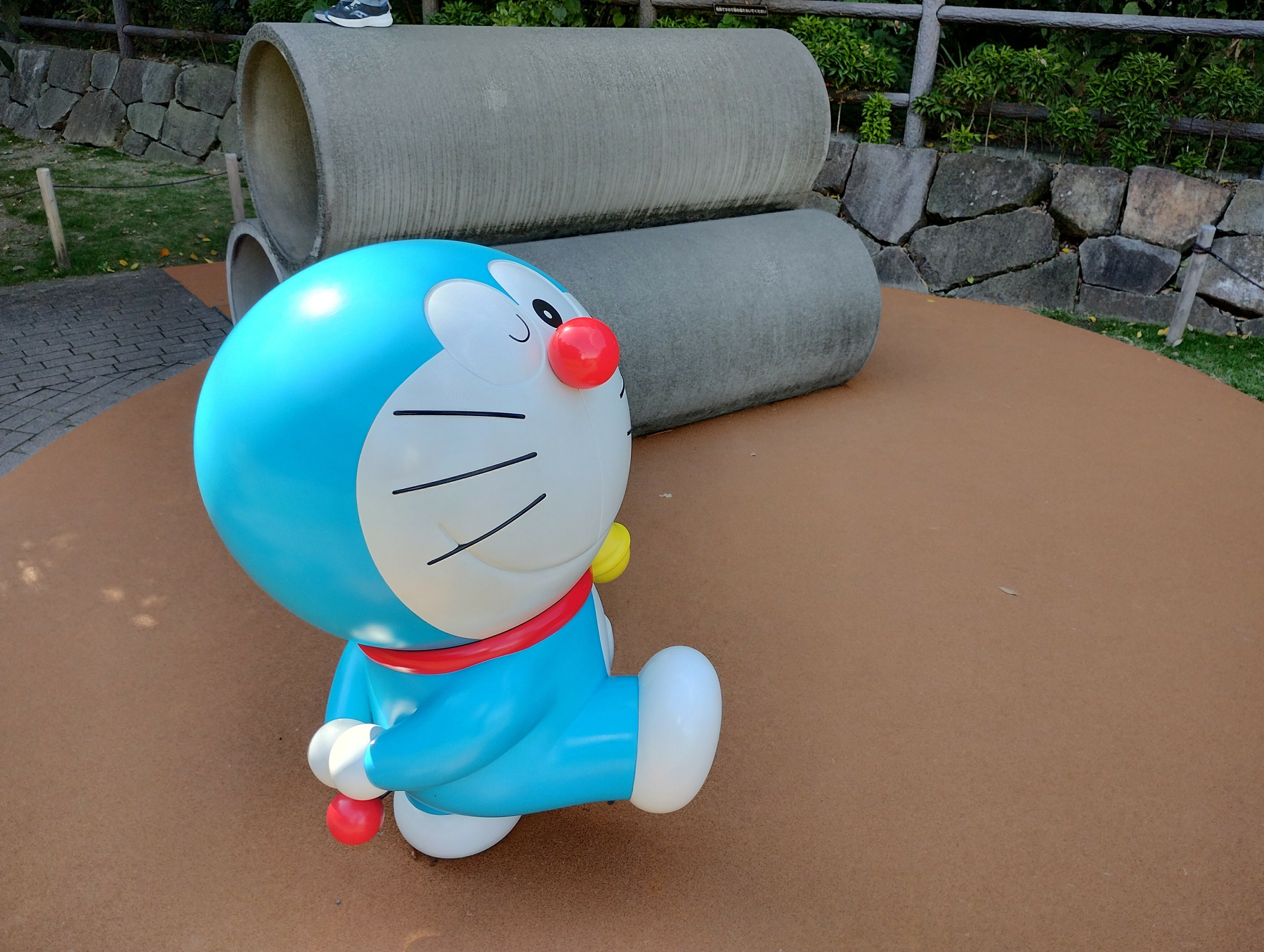 Auto-generated description: 赤い鼻を持つ青い猫型ロボットが屋外の遊び場に立っています。