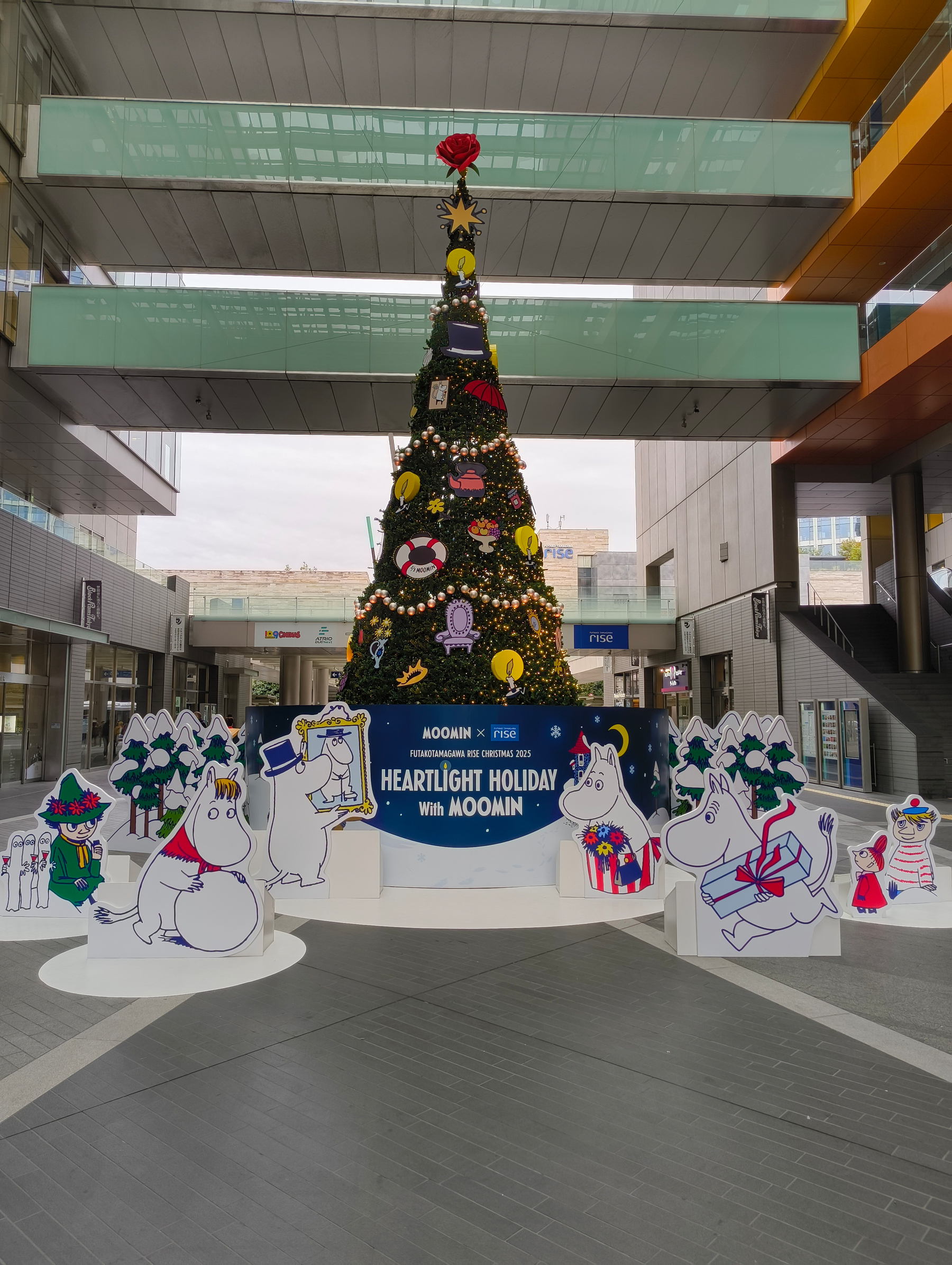 Auto-generated description: ムーミンのキャラクターが飾られたクリスマスツリーが、現代的な建物の中に展示されています。