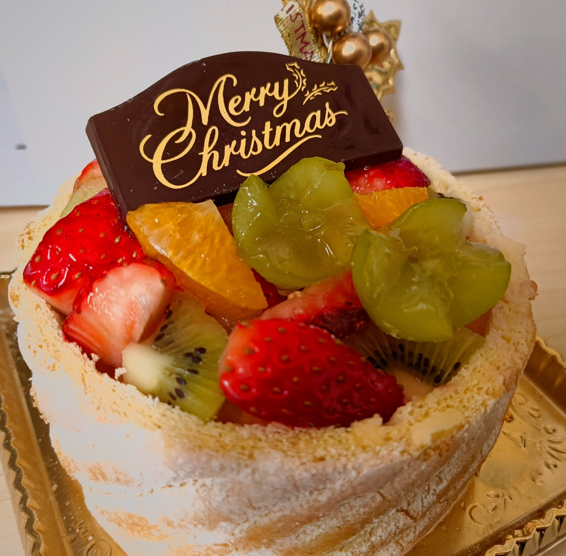 Auto-generated description: クリスマスデコレーションの載った果物たっぷりのケーキ。