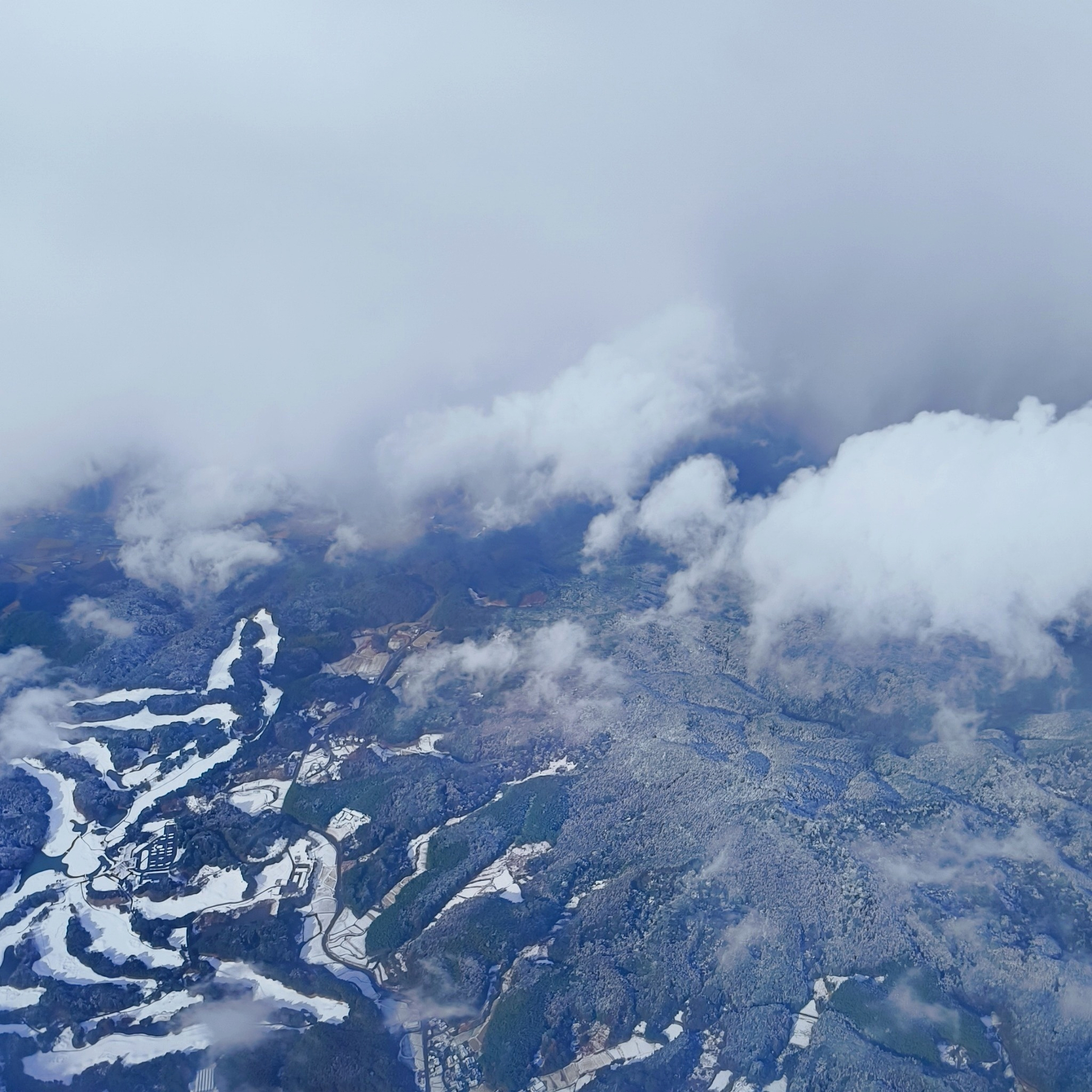 Auto-generated description: 上空から見た雲に覆われた雪景色の風景。