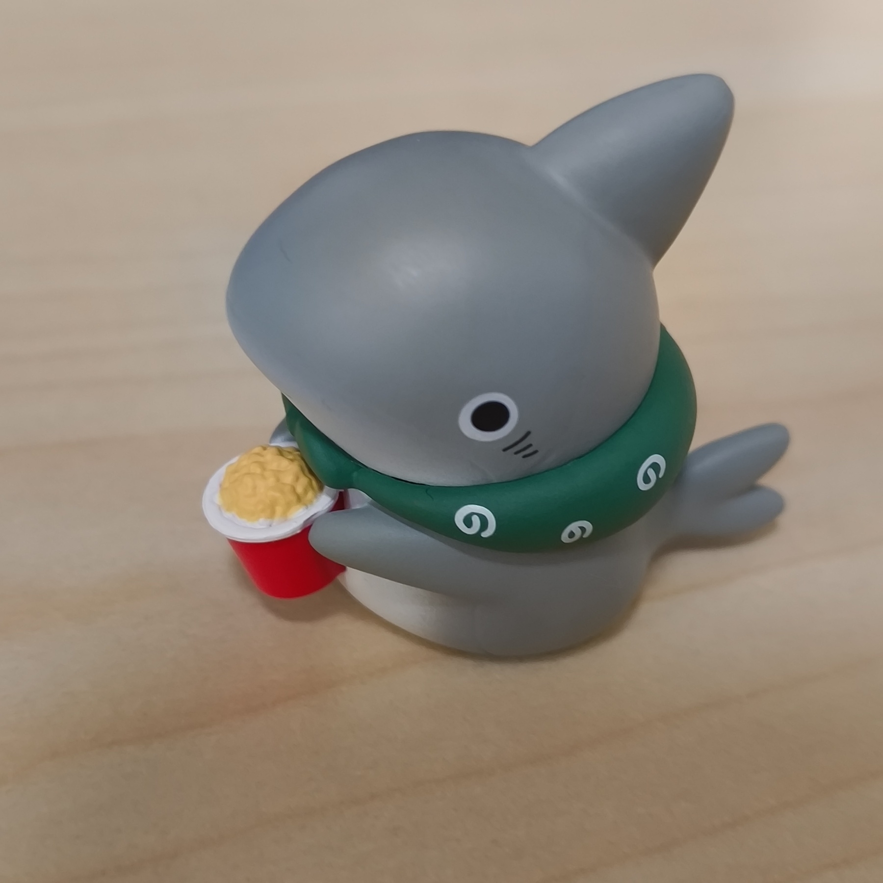 Auto-generated description: サメのフィギュアがスカーフを巻いて、カップに入ったポップコーンを持っています。