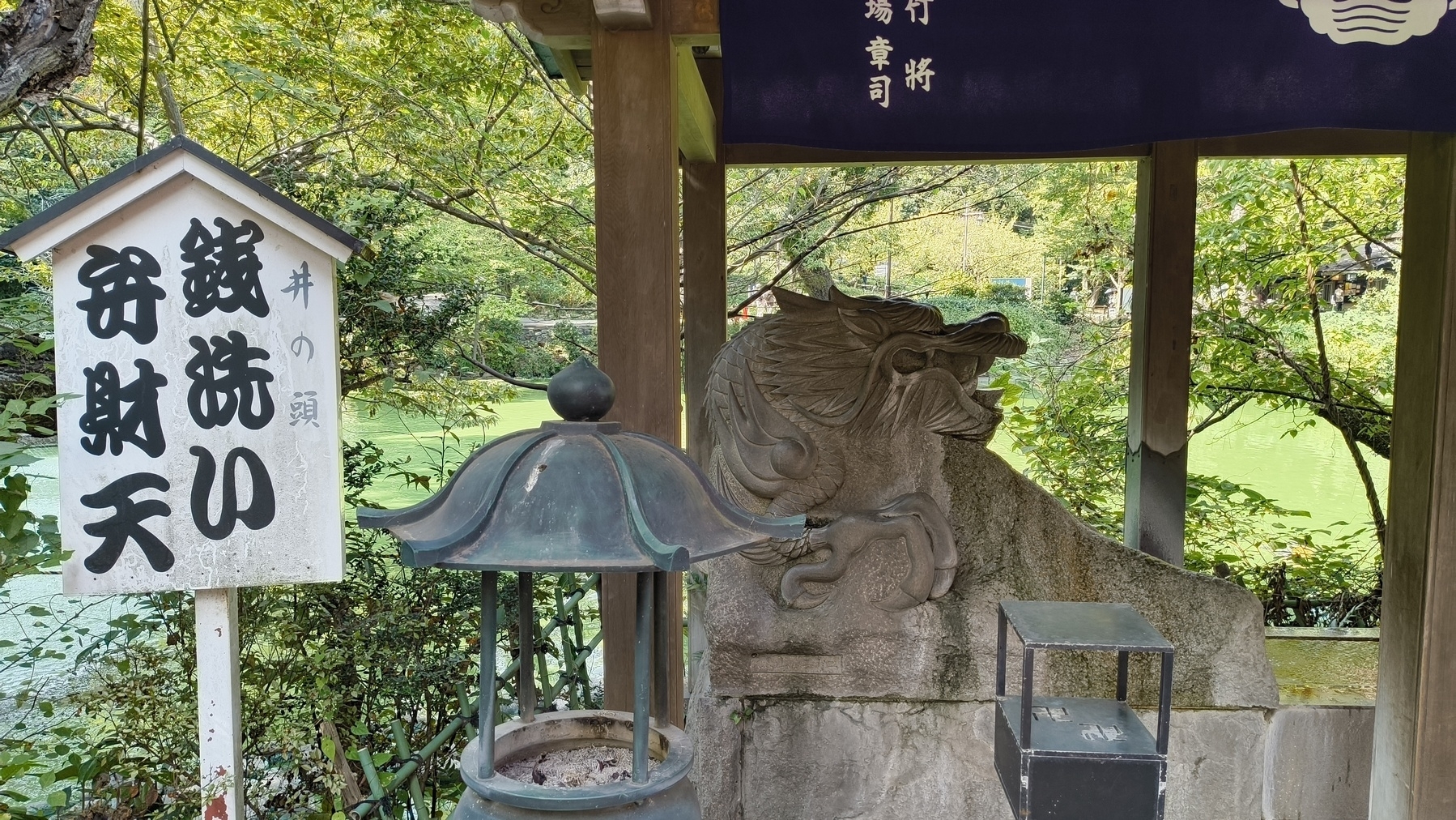 Auto-generated description: 銭洗い弁財天の看板と灯籠がある日本の庭園の風景。