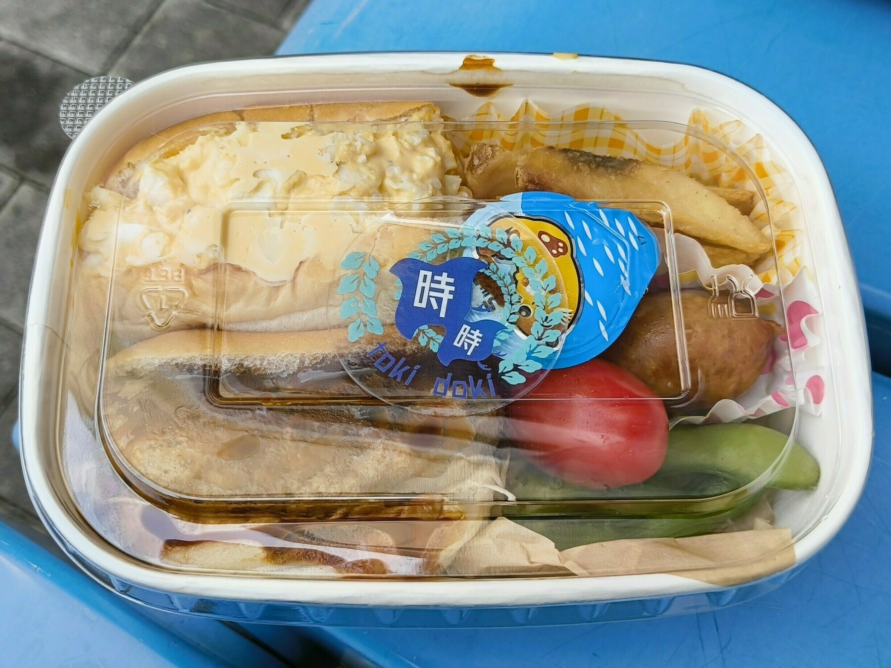 Auto-generated description: プラスチック容器にパン、ミニトマト、枝豆などが詰められた弁当。