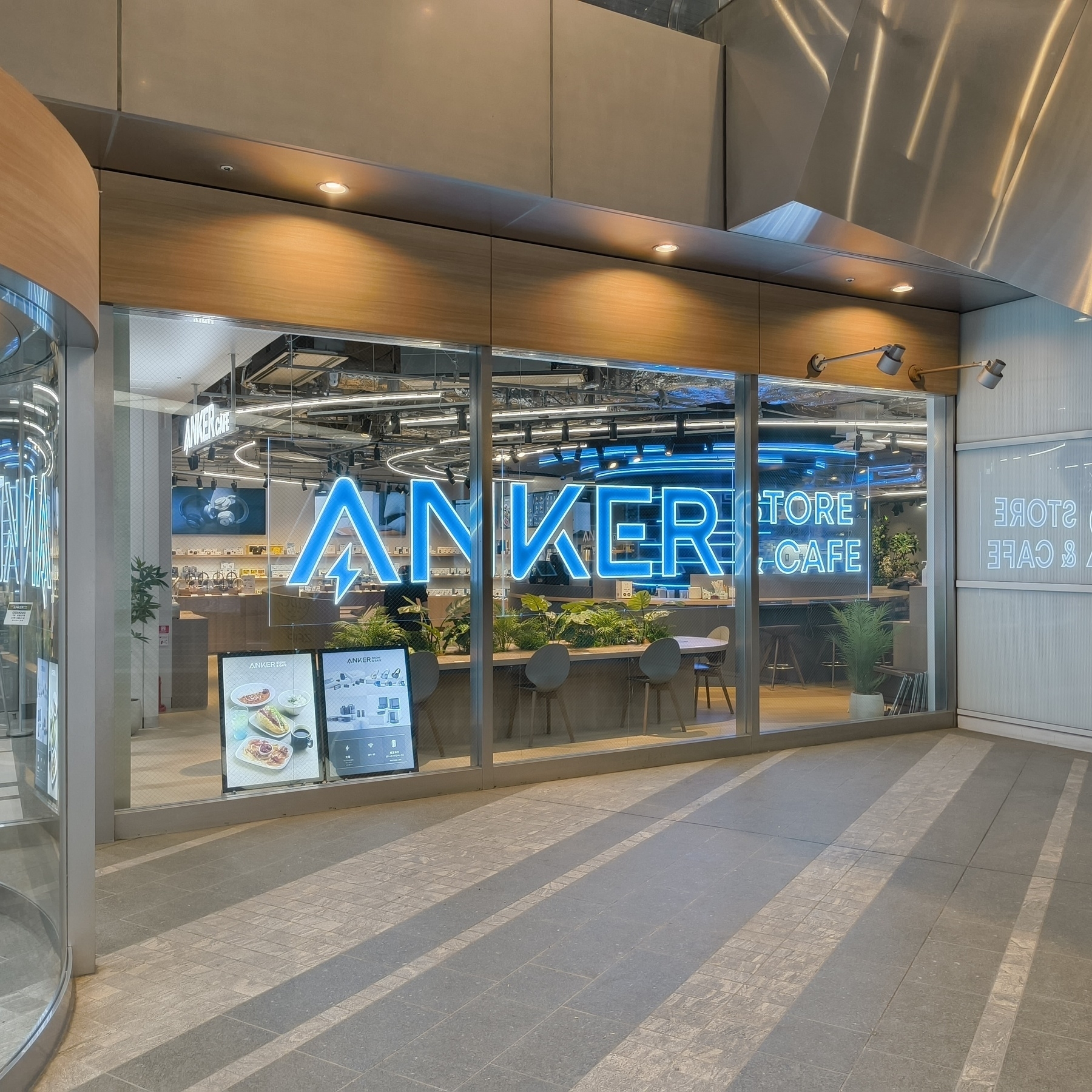 Auto-generated description: ANKERストアカフェの入口が大きなネオンサインで飾られており、店内には植物が配置されています。