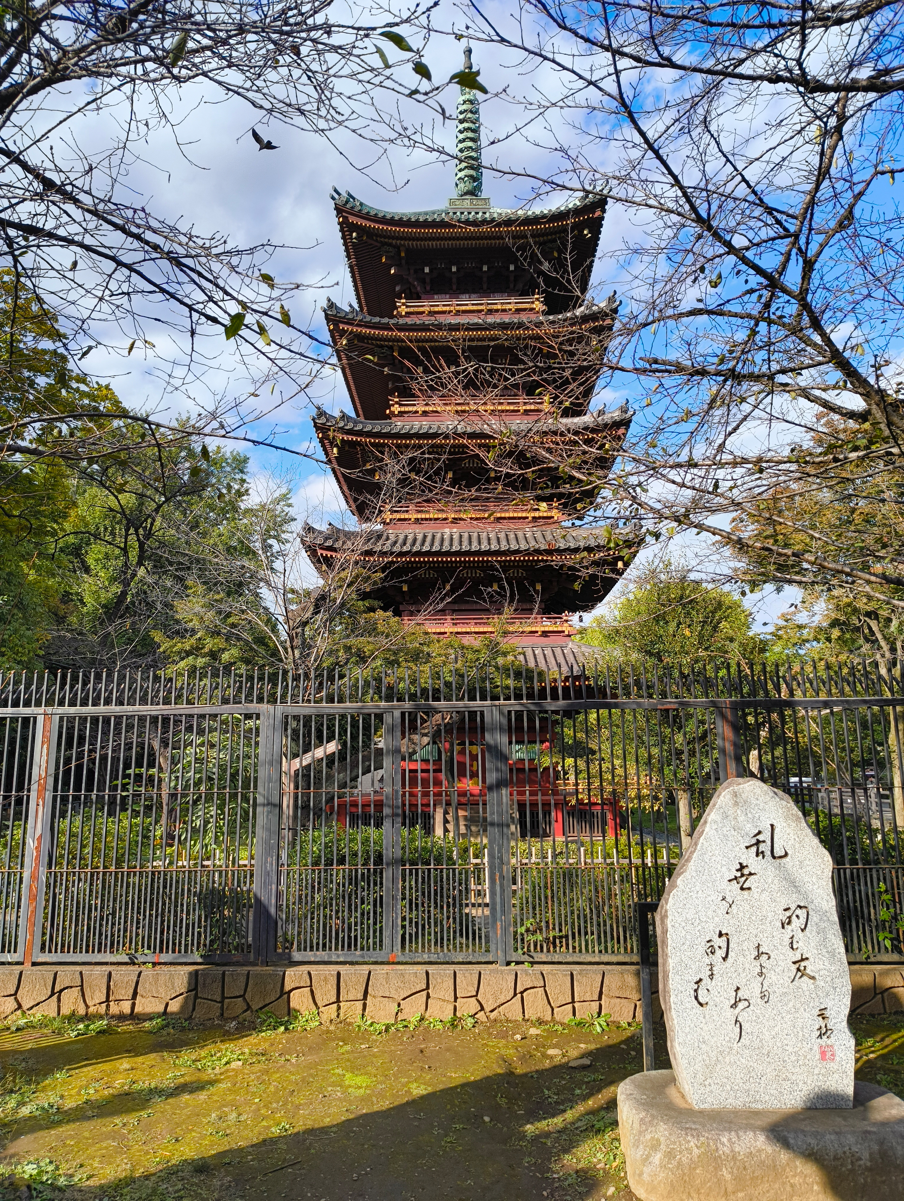 Auto-generated description: 5階建ての伝統的な日本の塔が木々に囲まれており、手前に石碑が立っています。