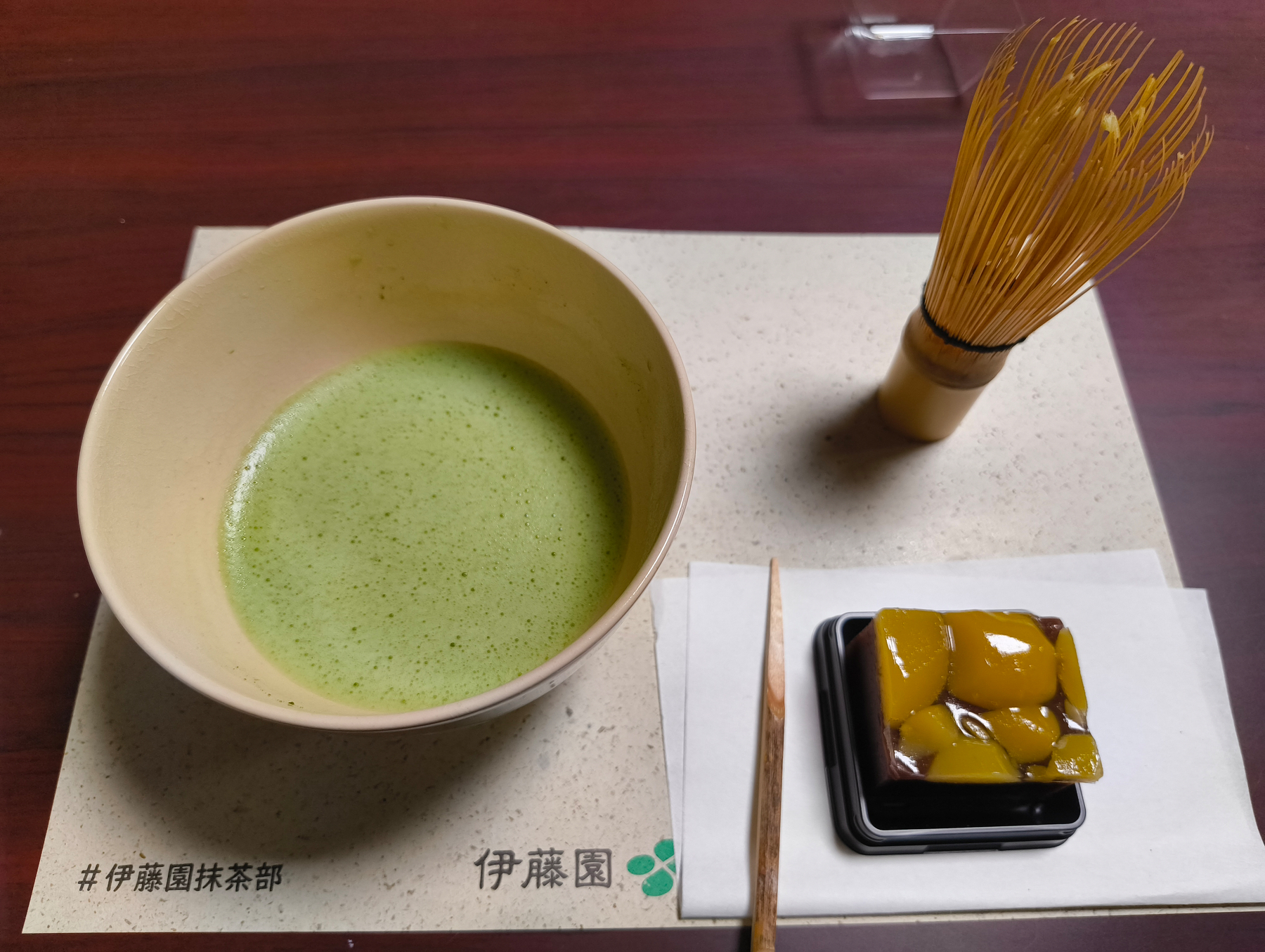 Auto-generated description: 抹茶と和菓子が畳の上に置かれ、茶筅が添えられています。