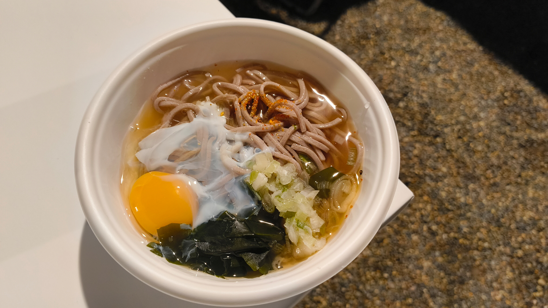 Auto-generated description: 白い容器に入ったそばには、生卵、ネギ、わかめが添えられています。　#青空ごはん部