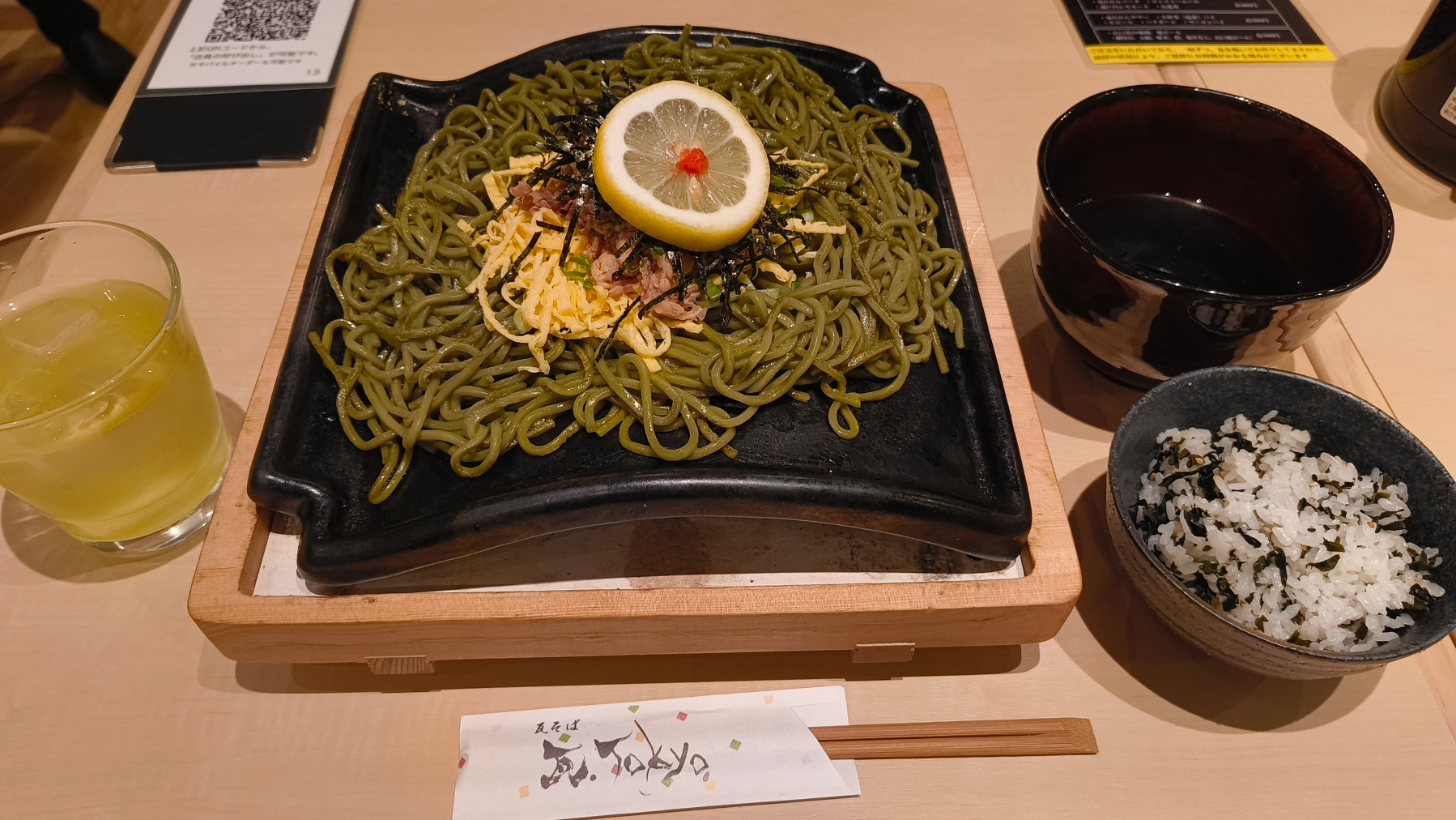 Auto-generated description: 麺の上にレモンともみじおろしが載せられたそばの料理が瓦に盛られ、わかめご飯とおつゆ、お茶が添えられた食事。