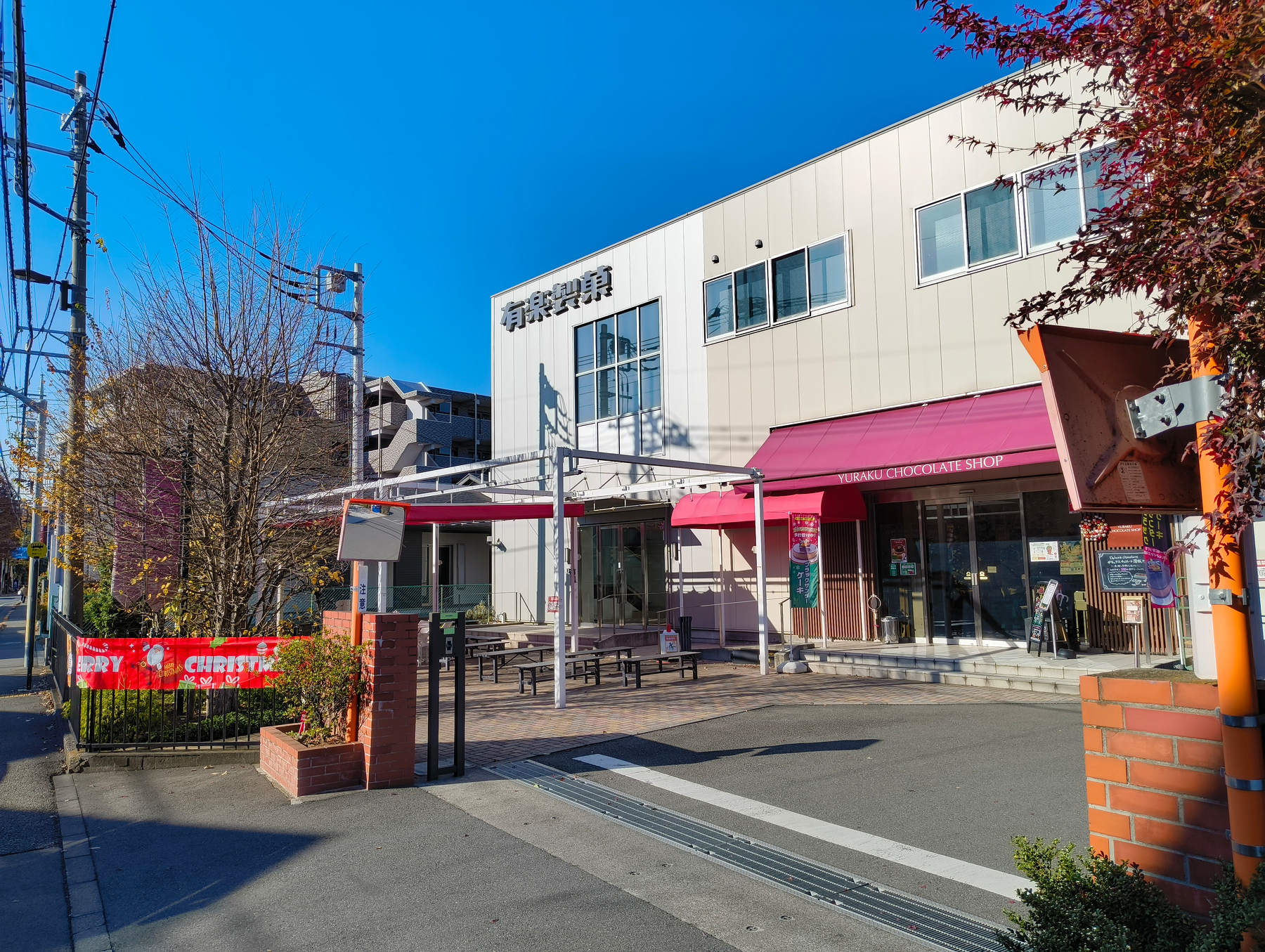 Auto-generated description: 日本の街角にある建物で、入口に赤い看板とベンチがある様子。