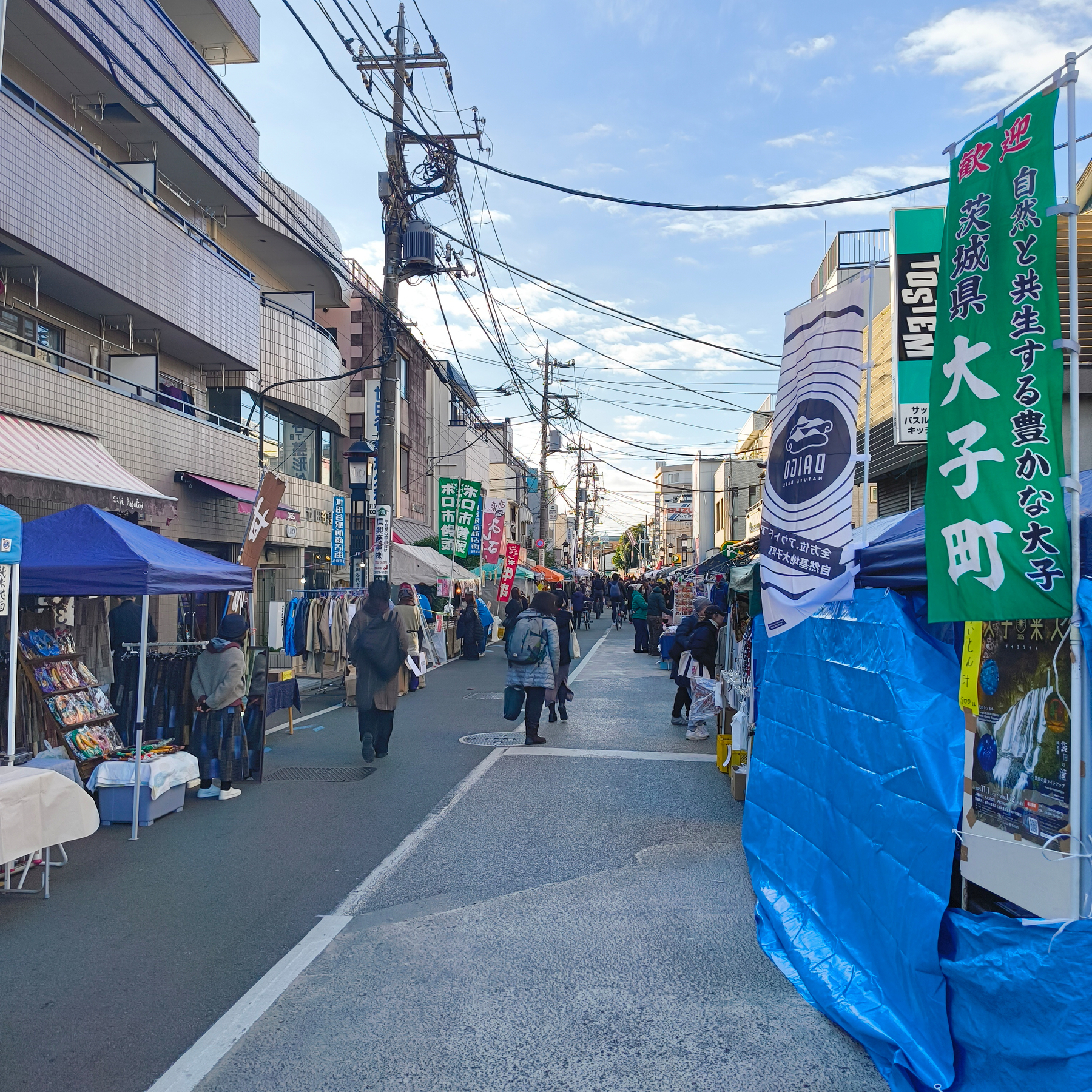 Auto-generated description: 商店街の両側に露店やテントが立ち並び、多くの人々が歩いている様子が見られる。