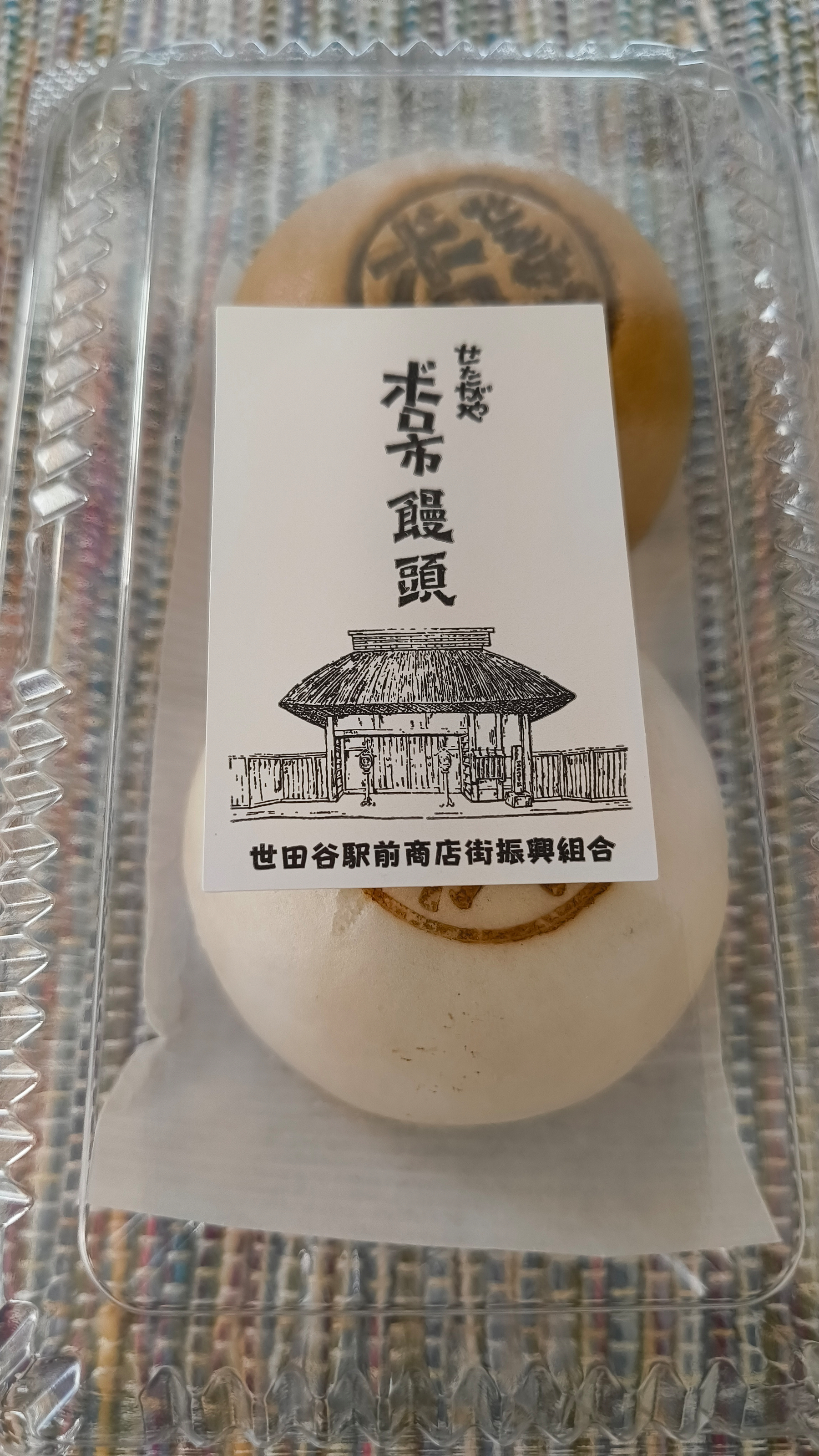 Auto-generated description: 透明なパッケージに入った2つの饅頭と、古い建物がイラストで描かれたラベルが見えます。