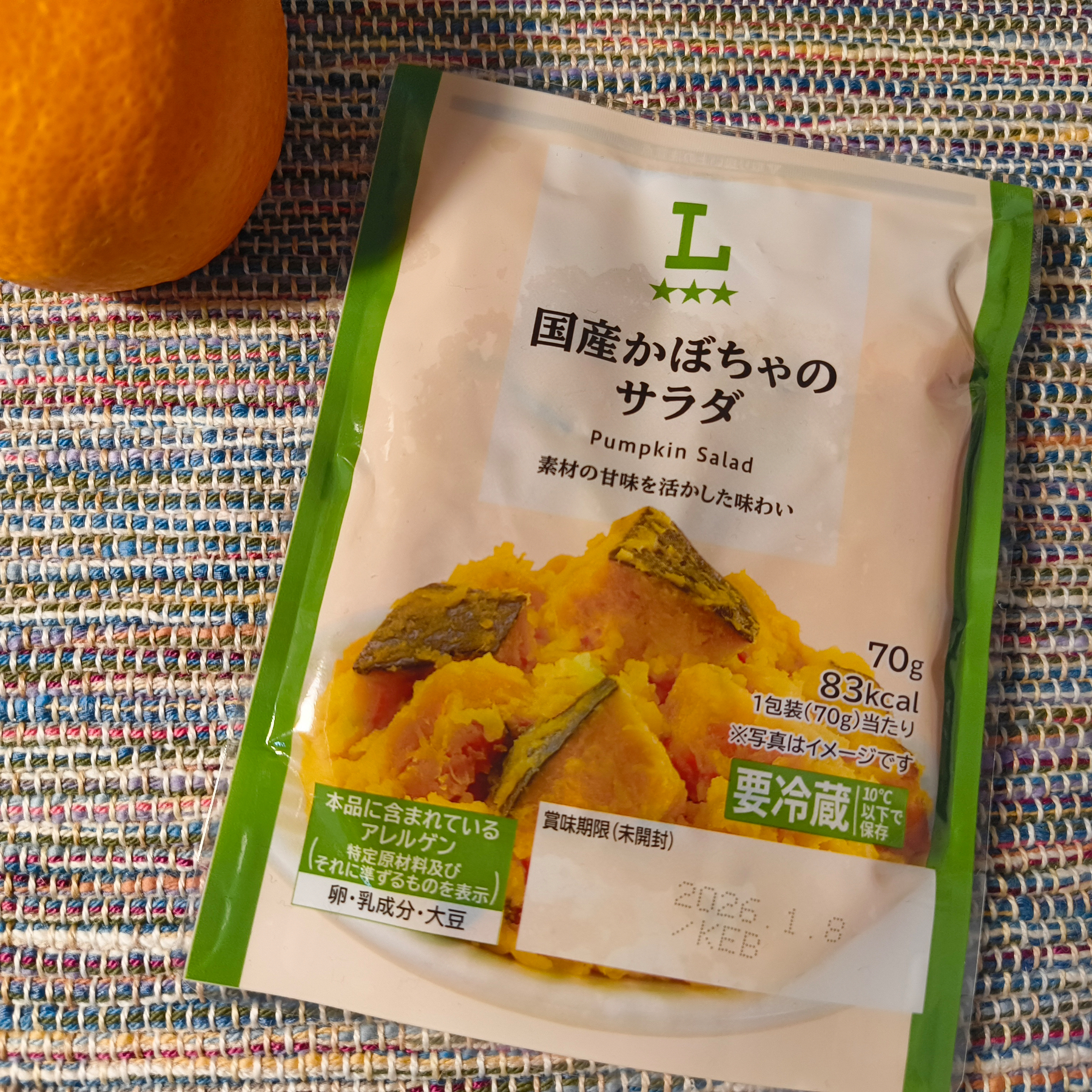 Auto-generated description: かぼちゃのサラダパックとオレンジがカラフルな布の上に置かれている。