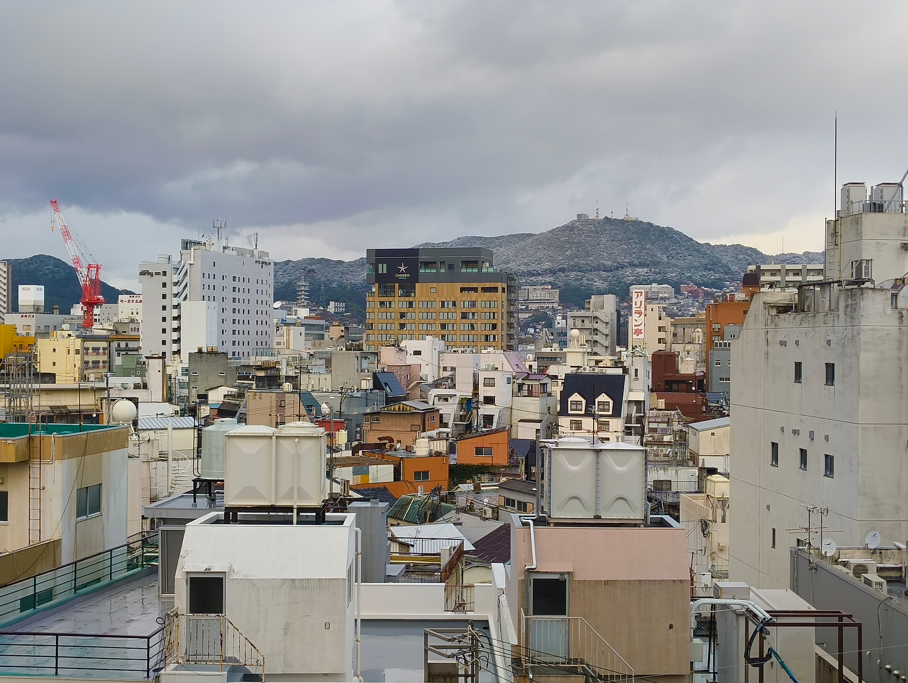 Auto-generated description: 山を背景に、多くの建物が立ち並ぶ都市の景色です。