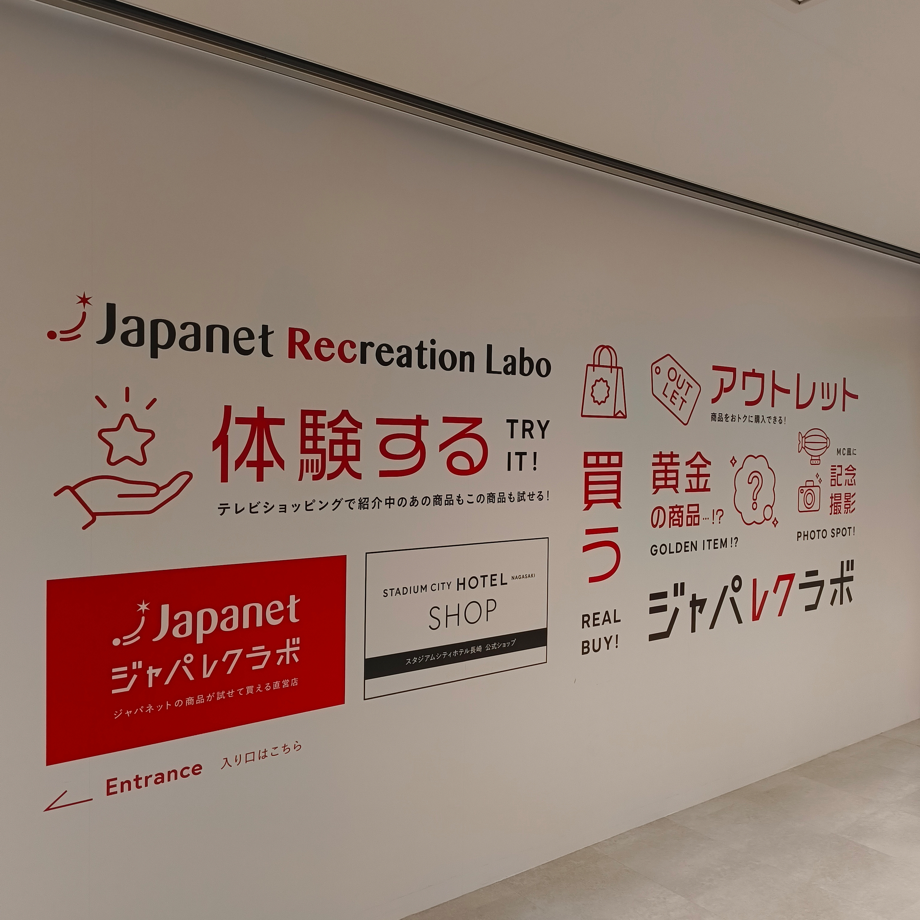 Auto-generated description: ジャパネットのロゴや文字でデザインされた店内の壁が写っています。