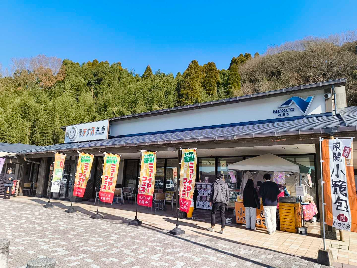 Auto-generated description: 道の駅にある店舗で、人々が商品の近くに立ち、カラフルな旗が並んでいます。