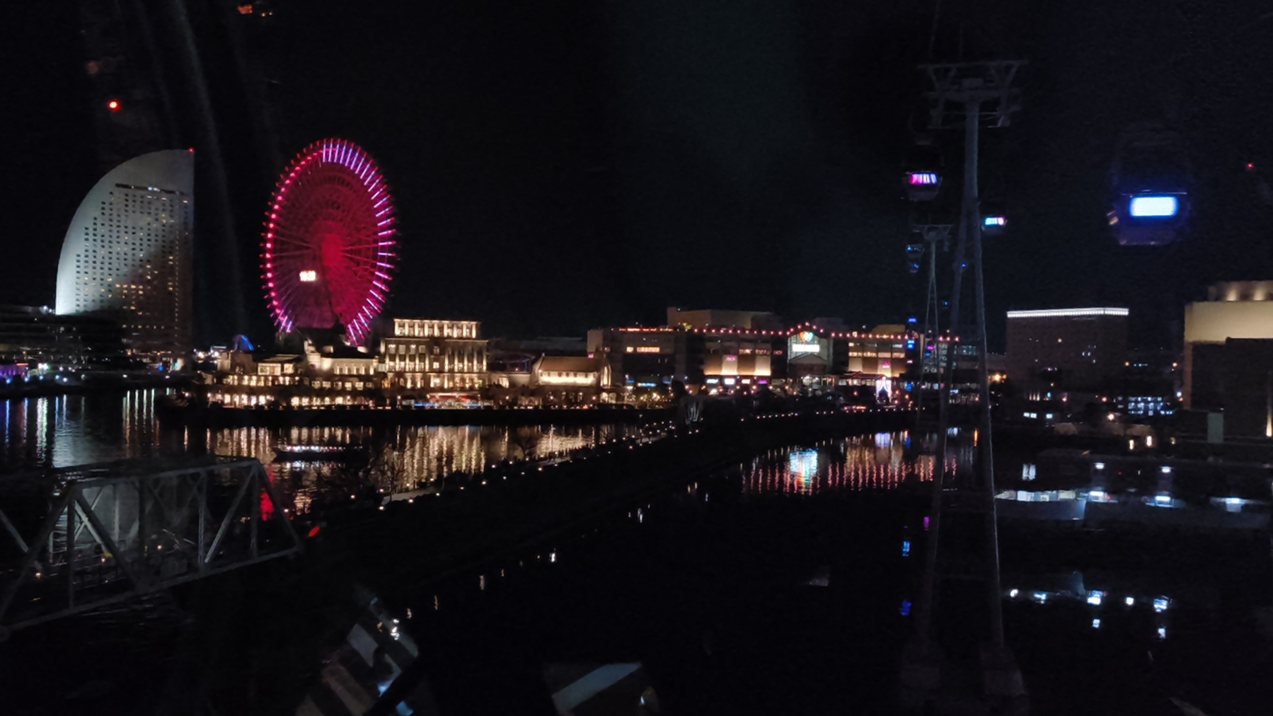 Auto-generated description: 観覧車と建物がライトアップされた夜の港の風景です。