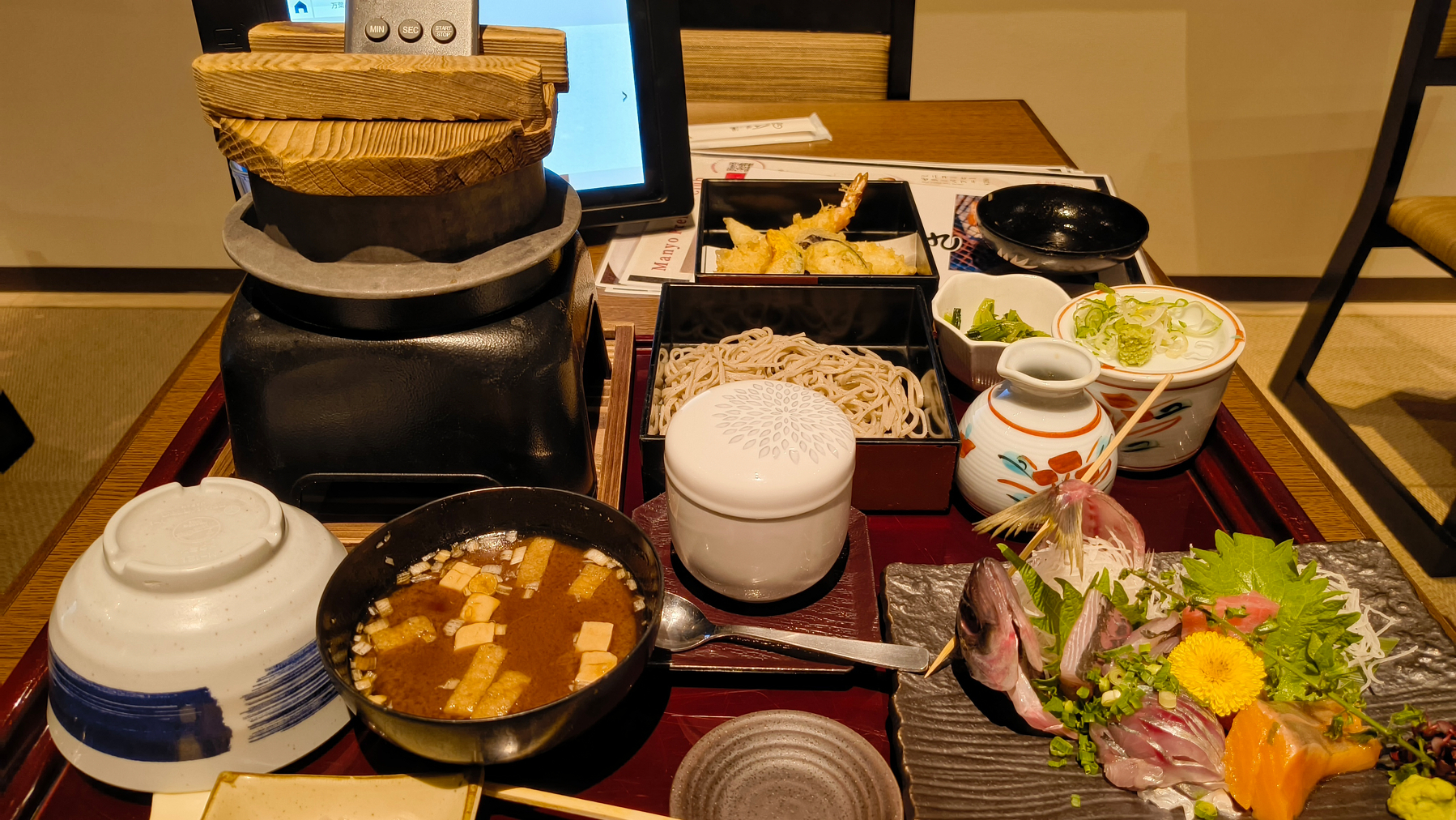 Auto-generated description: 日本料理の食卓には、天ぷら、蕎麦、刺身、味噌汁などの多様な料理が並んでいます。