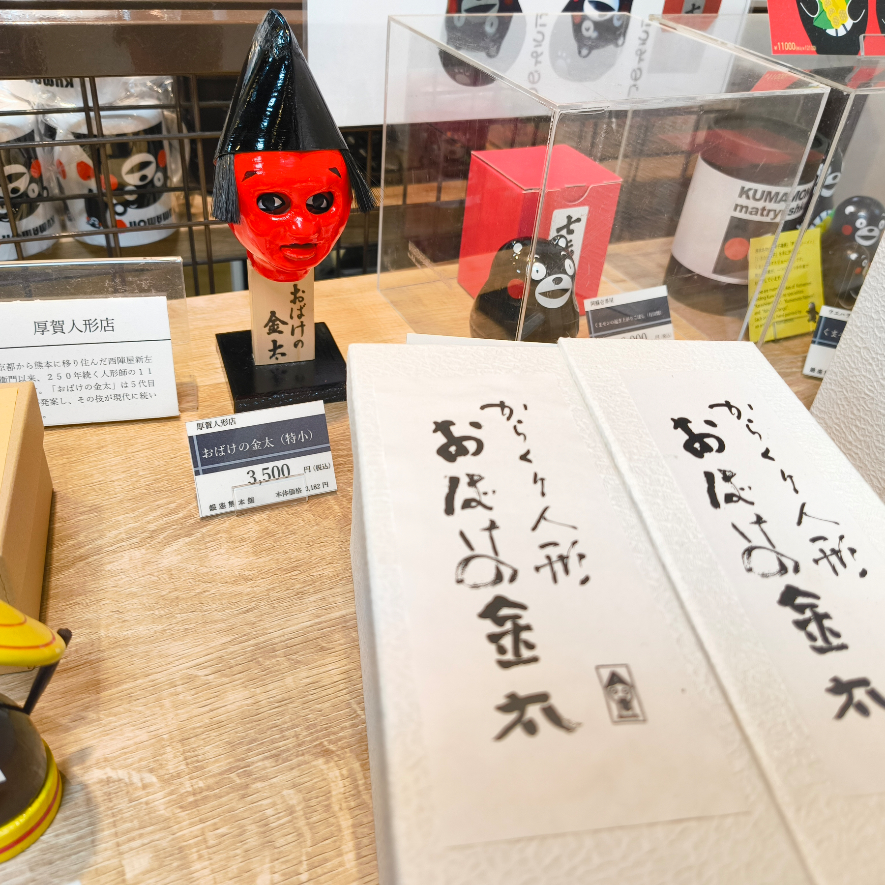 Auto-generated description: 赤い顔の置物と「おばけの金太」という文字が書かれた箱が陳列されている。
