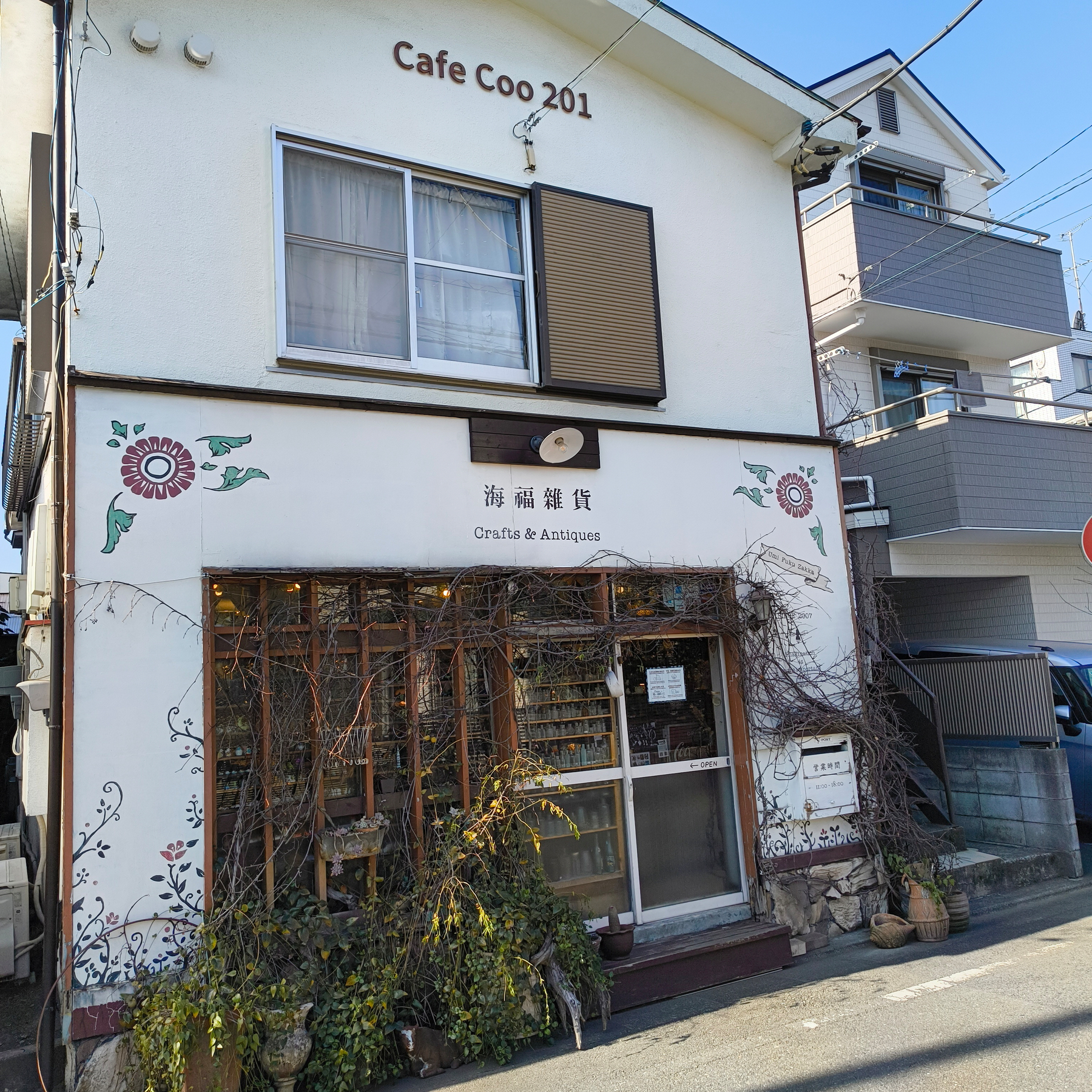 Auto-generated description: 「Cafe Coo 201」と書かれた看板がある白い建物に、ツタが巻きついた「海福雑貨」の店。