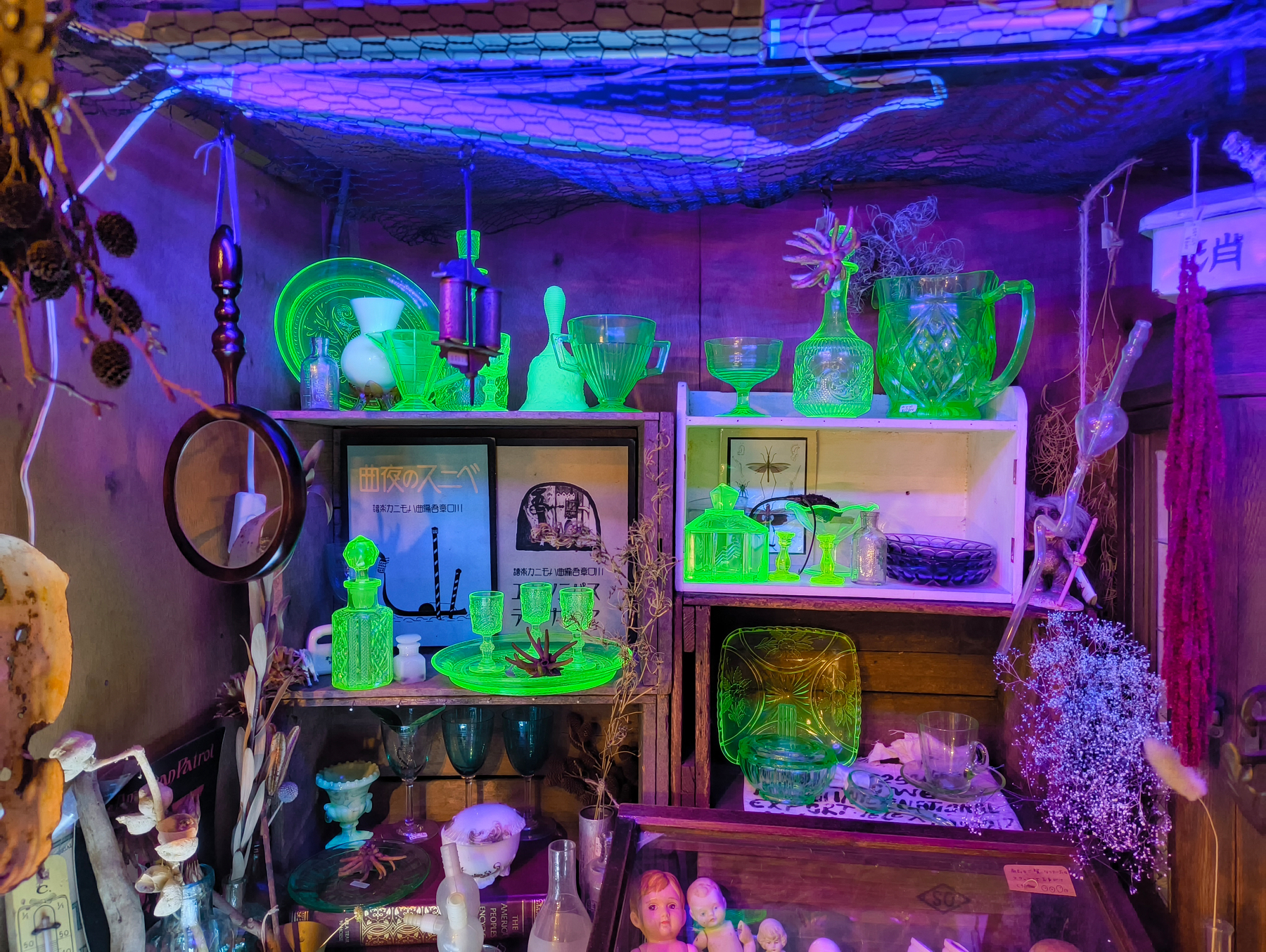Auto-generated description: 棚に緑色に光るウラングラスやさまざまな装飾品が並んでいる。