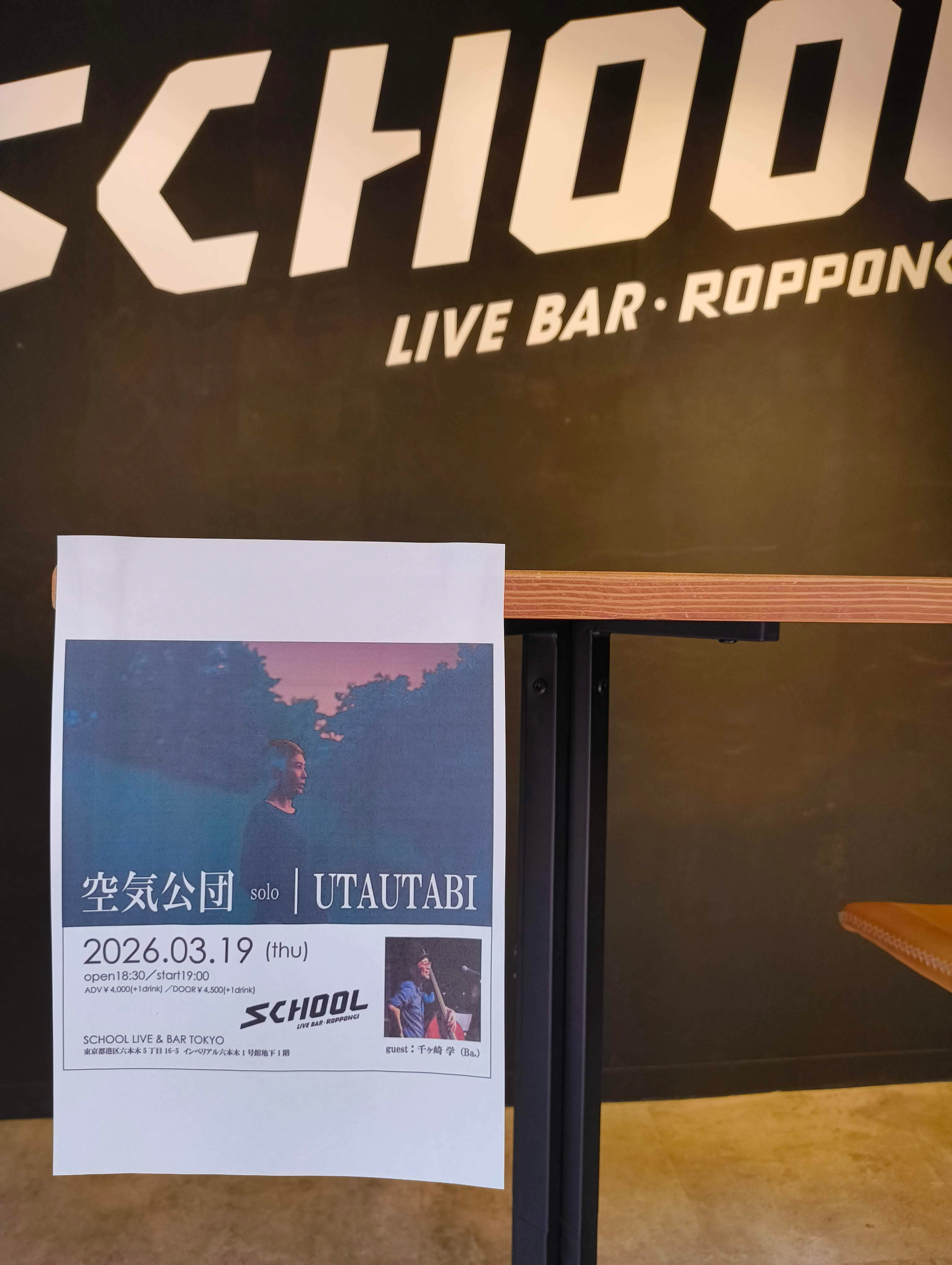 Auto-generated description: 六本木のライブバー「SCHOOL」で2026年3月19日に行われる「空気公団」ソロ「UTAUTABI」公演のチラシがテーブルに置かれている。