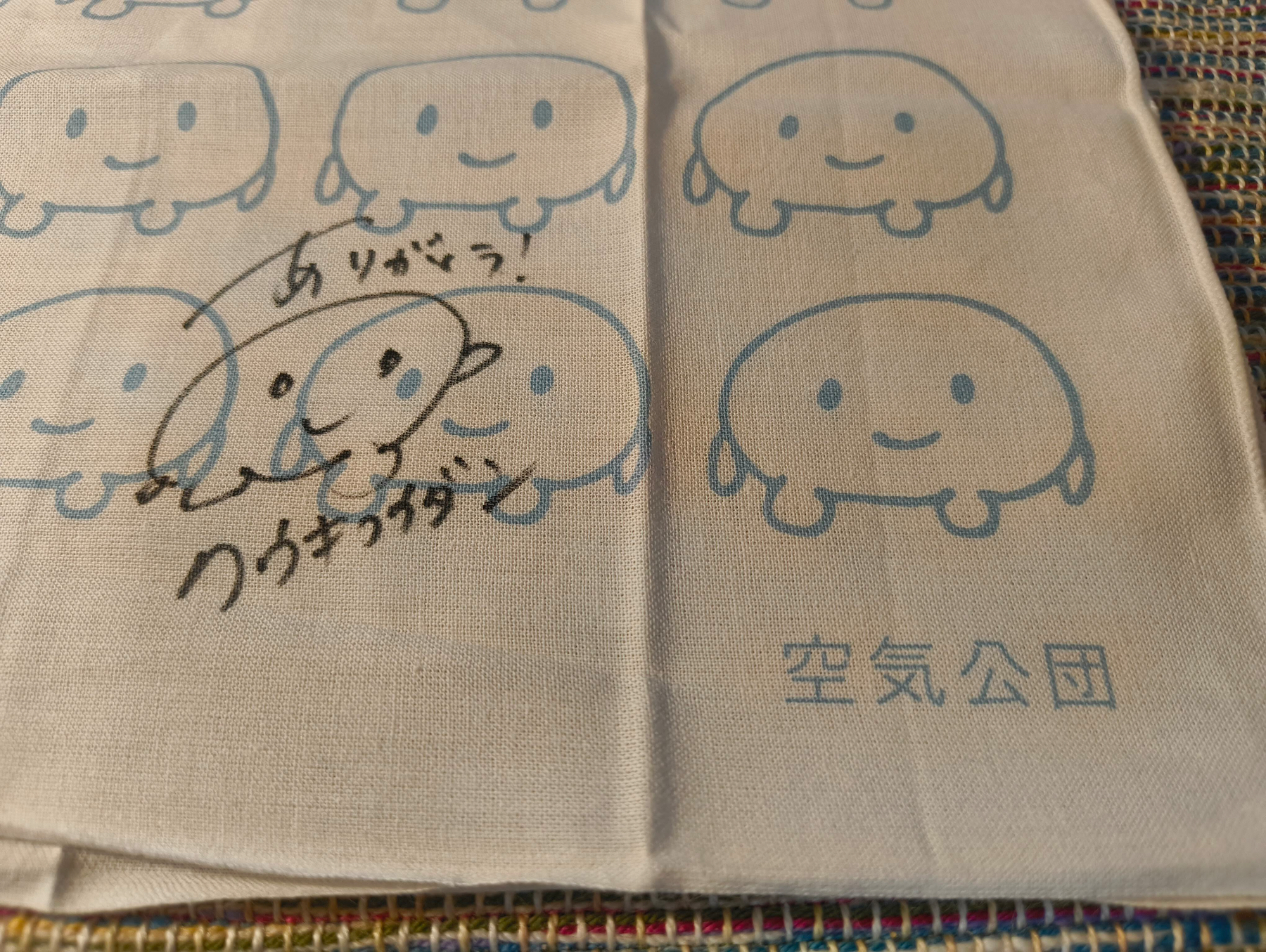 Auto-generated description: かわいいキャラクターが並んだ布地に、手書きのメッセージが書かれています。