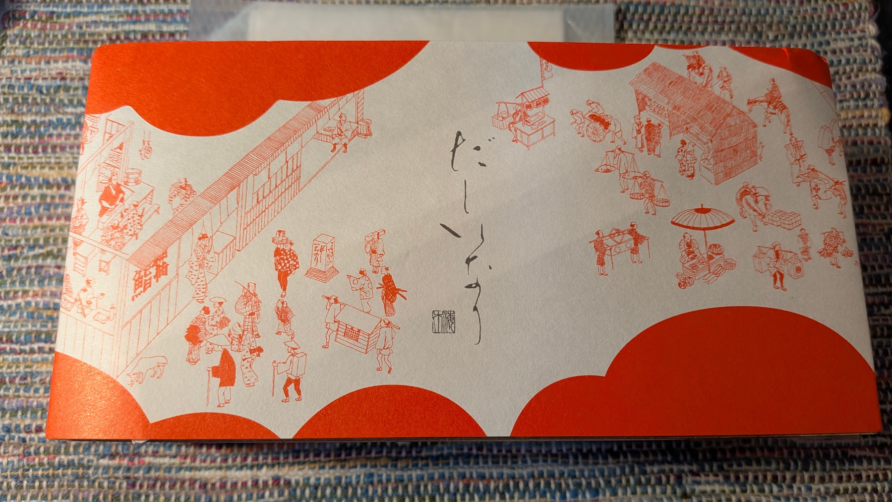 Auto-generated description: 和風の赤と白の包装紙に江戸時代の人々の生活風景が描かれている。